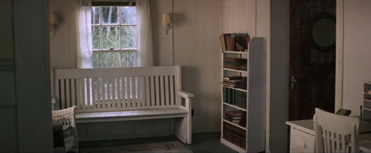 This Boy's Life (1993) movie still: wide — A quiet indoor space contains a white wooden bench and a small bookshelf. The room is empty with no…