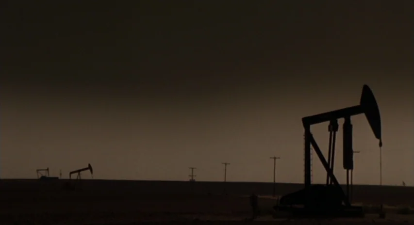 Blood Simple (1984) movie still: wide — A vast, barren oil field stretches toward a dark, overcast horizon line. Several mechanical oil pump jacks…