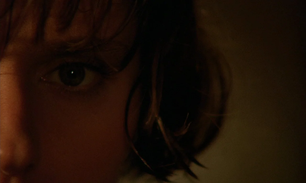 The Church (1989) movie still: closeup — A dimly lit interior space with shadows obscuring most of the frame. A person's eye and partial face are…