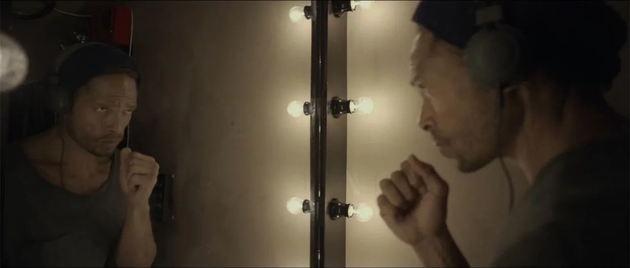 All She Wrote (2018) movie still: medium — A dressing room features a mirror surrounded by vertical rows of vanity light bulbs. A man wearing…