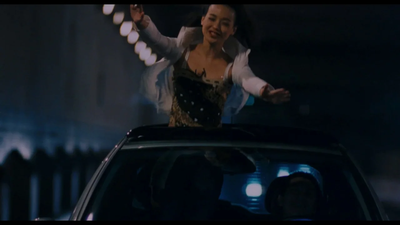 Millennium Mambo (2001) movie still: medium — A woman stands up through the open sunroof of a car moving inside a tunnel. The tunnel walls feature a…