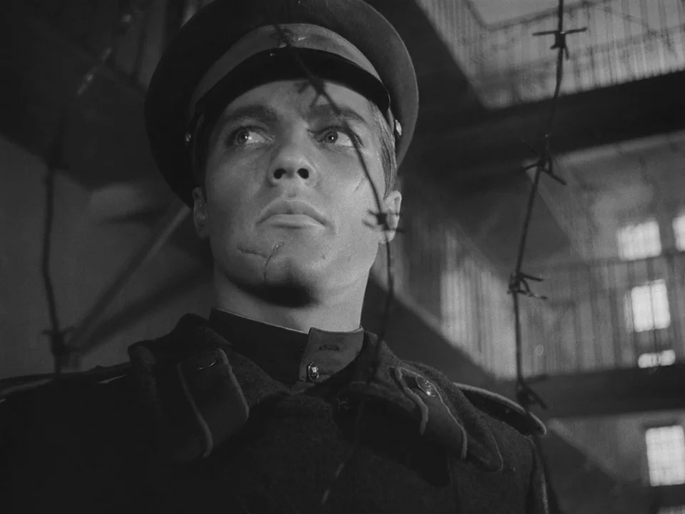 Ivan’s Childhood (1962) movie still: closeup — A dark interior with multi-level metal stairs and railings visible in the background. A man in a…