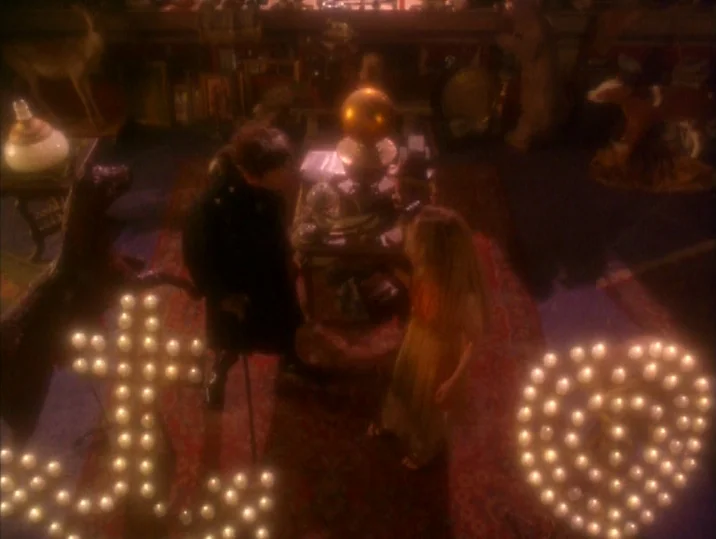 Twilight of the Ice Nymphs (1997) movie still: wide — A dark, cluttered room is filled with antique figurines and various objects on shelves. A man…