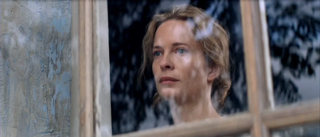 The Banishment (2007) movie still: closeup — A woman stands behind a glass window with dark silhouettes visible in the reflection. She looks ahead…