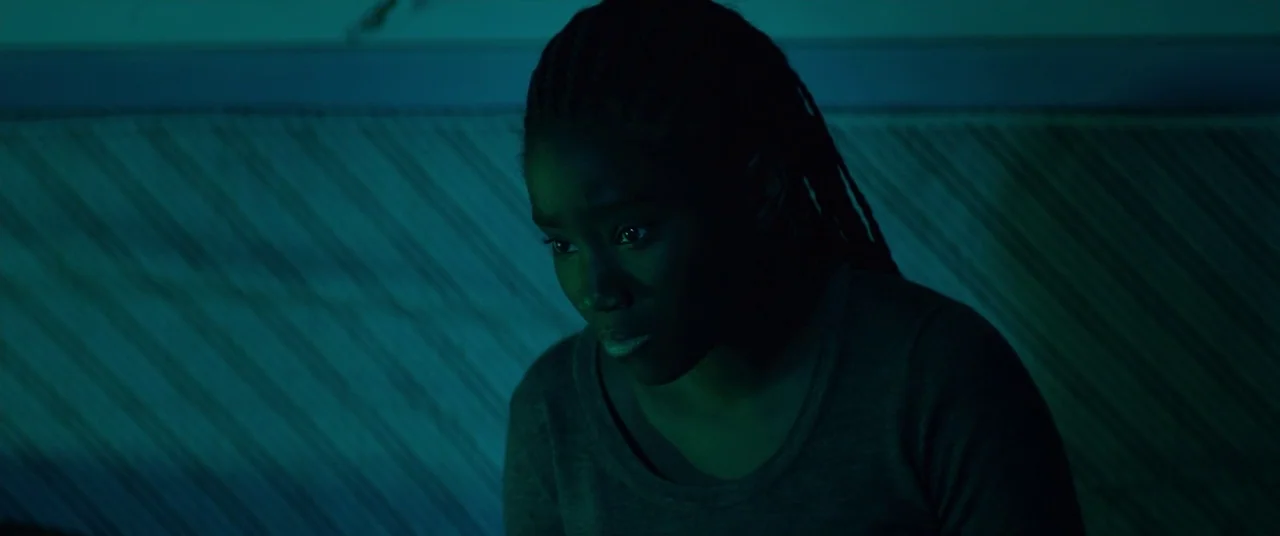 Girlhood (2014) movie still: closeup — A dimly lit room features a woman illuminated by an off-screen digital display. The subject stares downward…