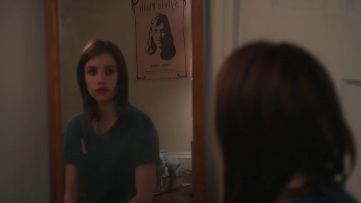 Adult World (2013) movie still: medium — A bathroom mirror shows a woman staring at herself while a poster hangs nearby. The woman looks at her…
