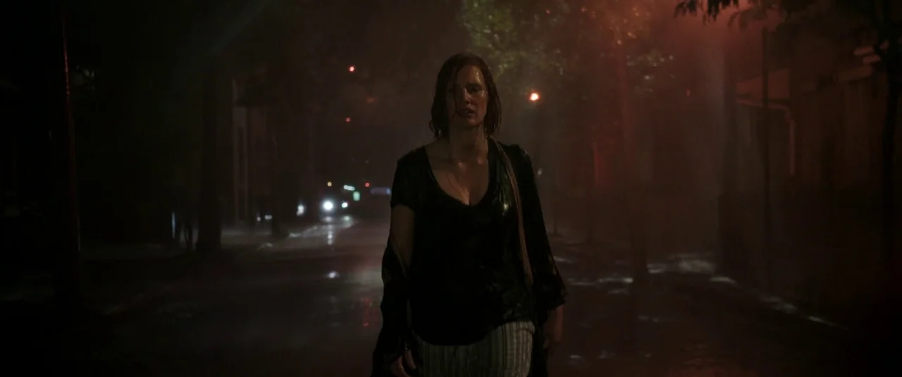 It Chapter Two (2019) movie still: medium — A dark, rain-slicked city street at night is illuminated by distant flickering lights. A woman with wet…