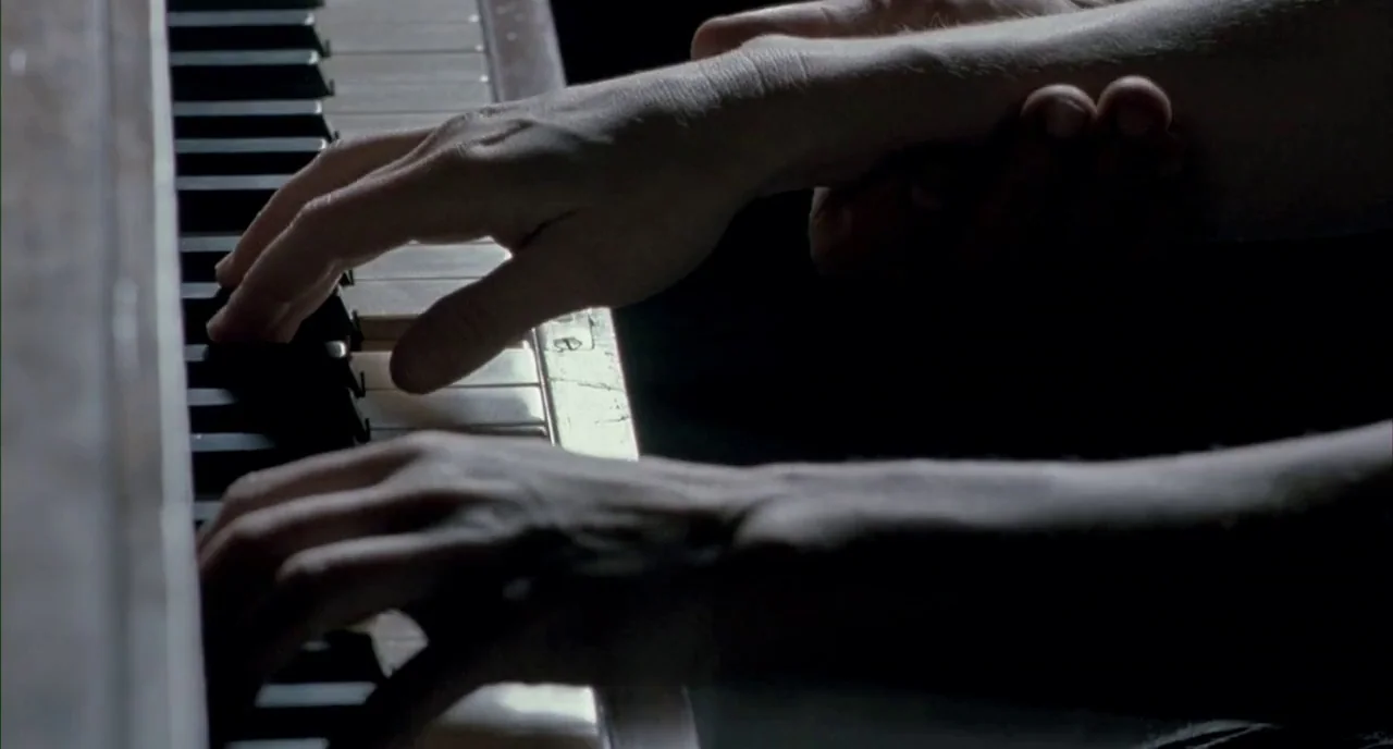 The Piano (1993) movie still: closeup — A close-up shows two sets of hands resting on the black and white piano keys. One hand holds the wrist of…