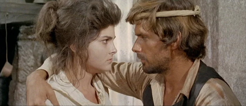 Django Kill (1967) movie still: medium — A rustic interior with textured stone walls provides a backdrop for two people. A man and woman stand close…