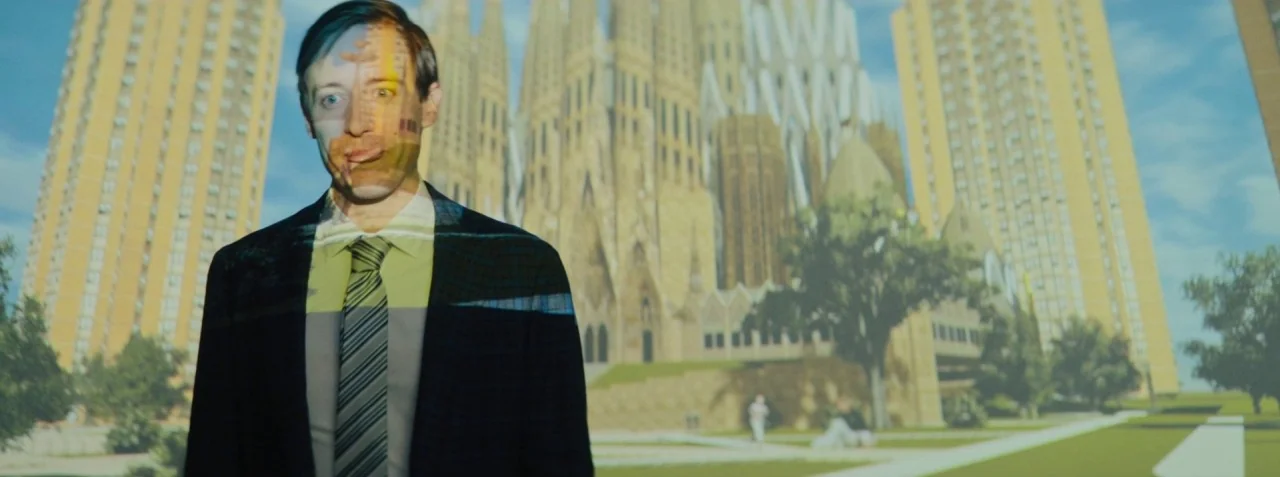 Dead Pigs (2018) movie still: medium — A man stands in a dark room with a large projection of architecture behind him. The projected light overlays…