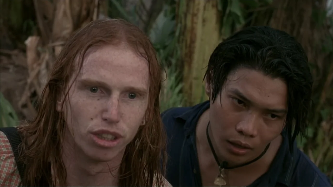 Behind Enemy Lines (2001) movie still: medium — A dense tropical jungle environment featuring tall banana leaves and blurred foliage. Two young men…