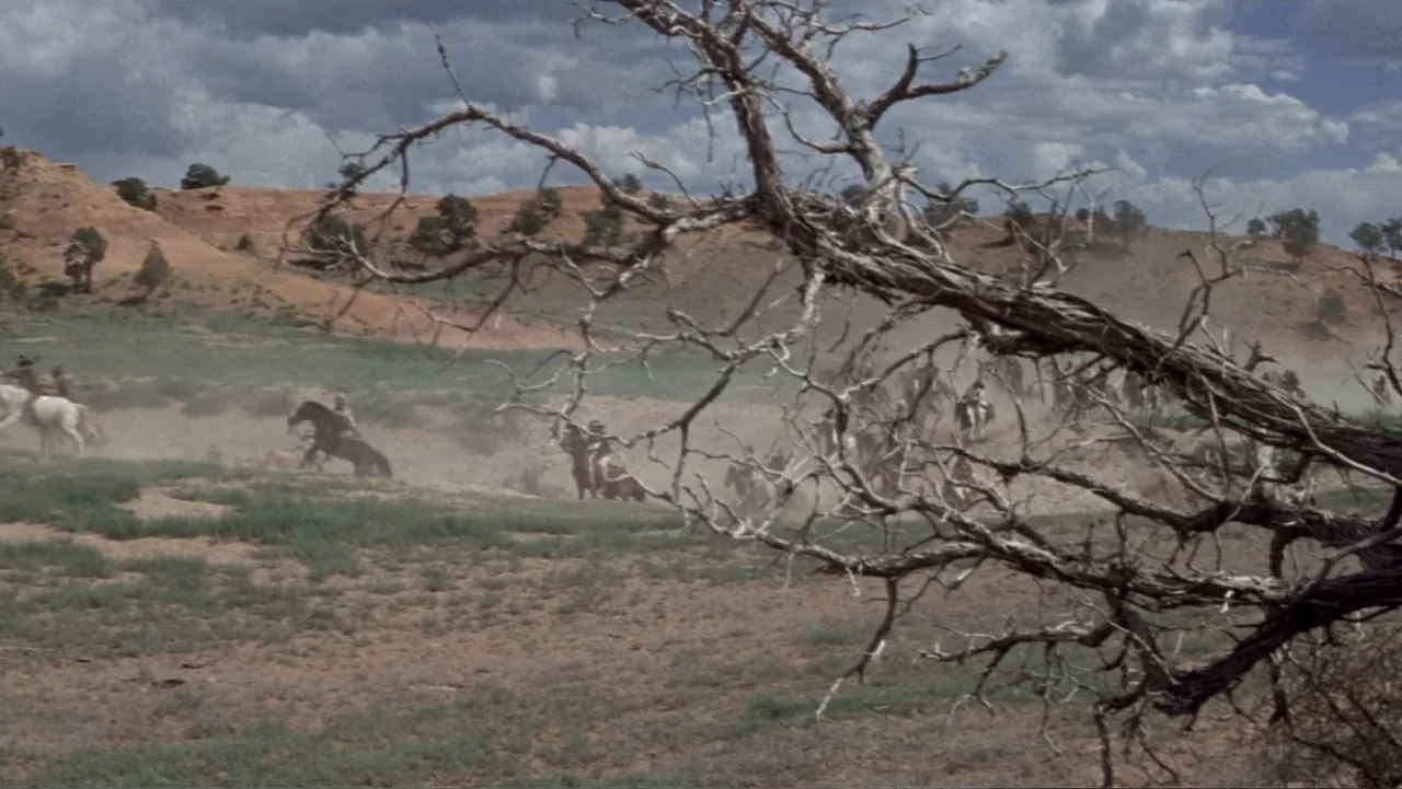 A Distant Trumpet (1964) movie still: wide — A vast, arid desert landscape features rolling hills and sparse vegetation under a cloudy sky. A small…