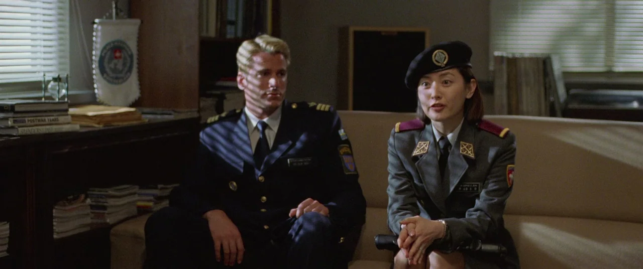 Joint Security Area (2000) movie still: medium — An office interior features Venetian blinds casting shadows across a man and a woman. Both figures…