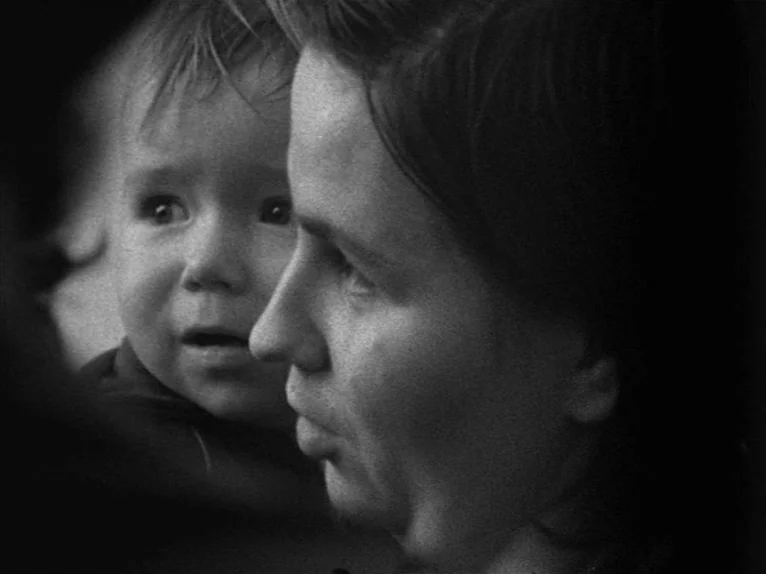 Family Nest (1979) movie still: closeup — A close up view focuses on a woman and a baby in low lighting. The mother looks straight ahead while the…