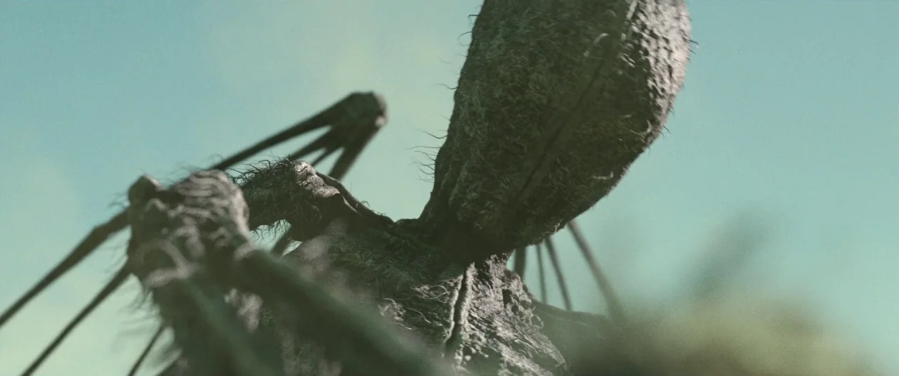 Southbound (2015) movie still: closeup — A tall, textured, humanoid figure stands in an open area under a clear sky. The creature features a rough,…