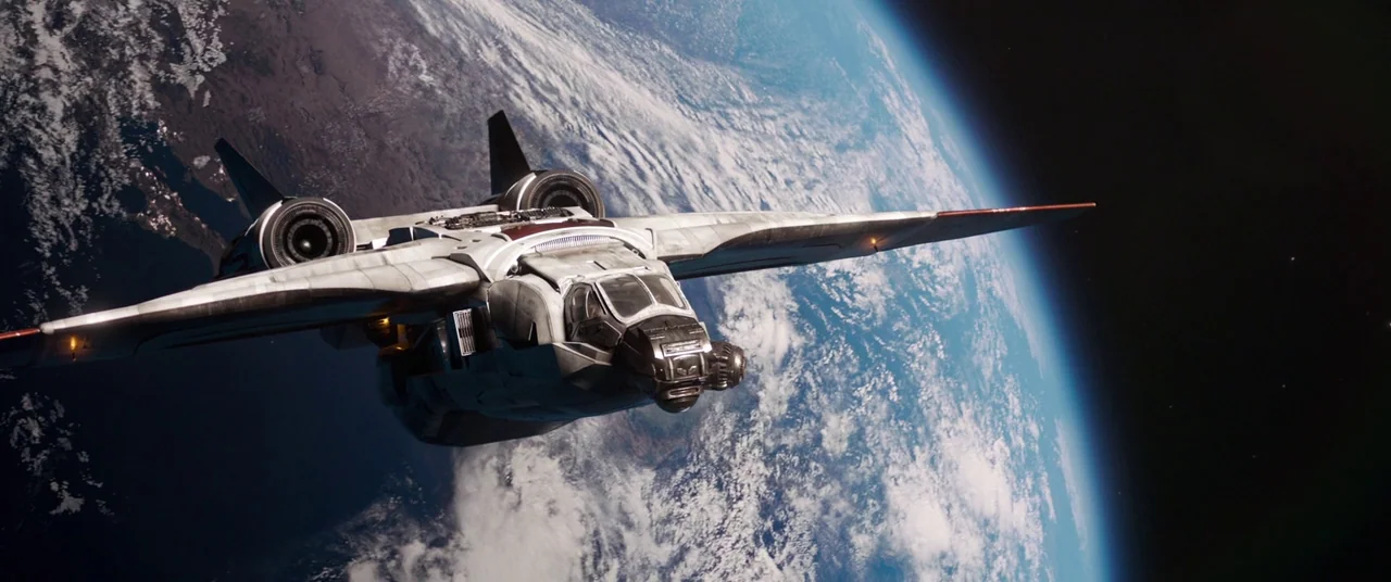 Captain Marvel (2019) movie still: wide — A metallic spacecraft flies through the vacuum of space above a planet. Earth's blue atmosphere and white…