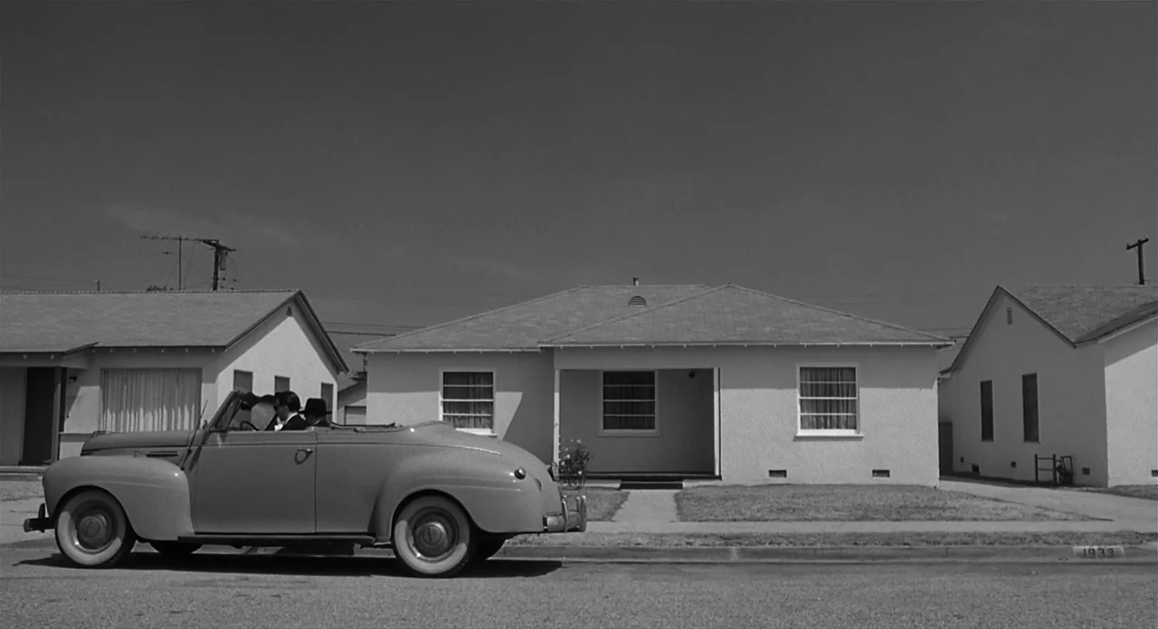 Ed Wood (1994) movie still: wide — A residential street features three minimalist single-story houses under a cloudless midday sky. A vintage…