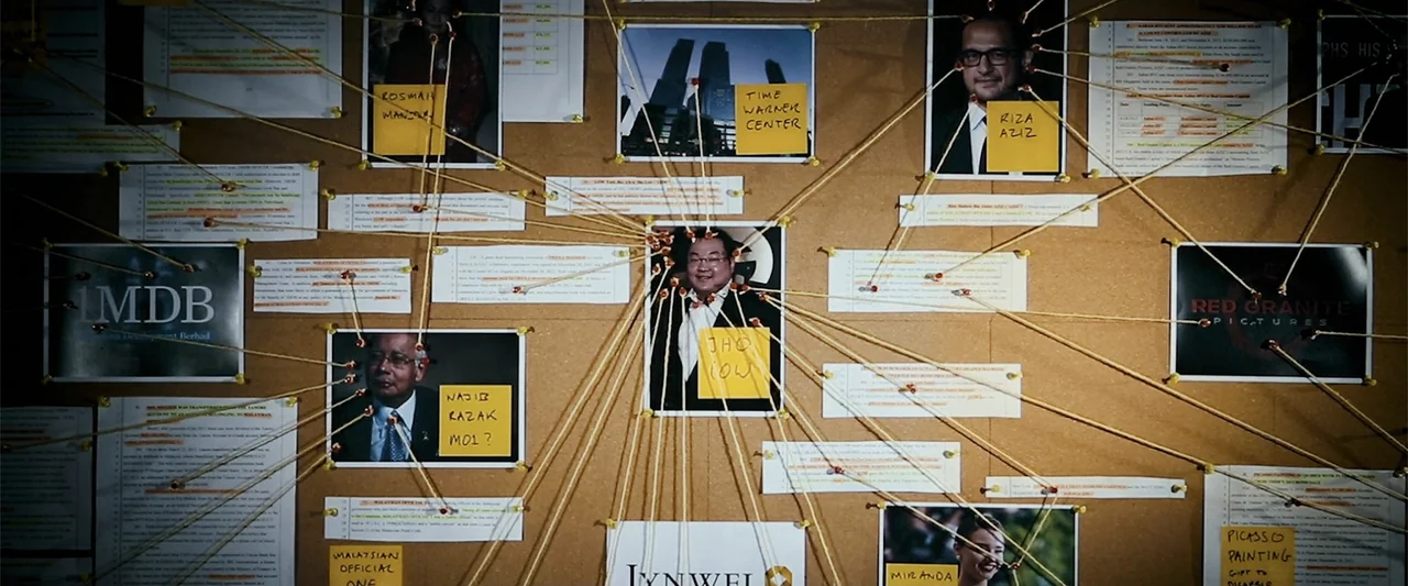 The Kleptocrats (2018) movie still: wide — A dark cork board is covered with multiple photographs, documents, and yellow sticky notes. Yellow string…
