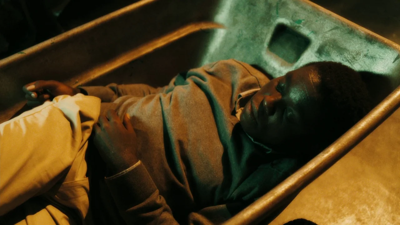 Saw VI movie still: medium — A dark, cramped morgue setting features a metallic basin used for storage. A man lies motionless in the basin with his…