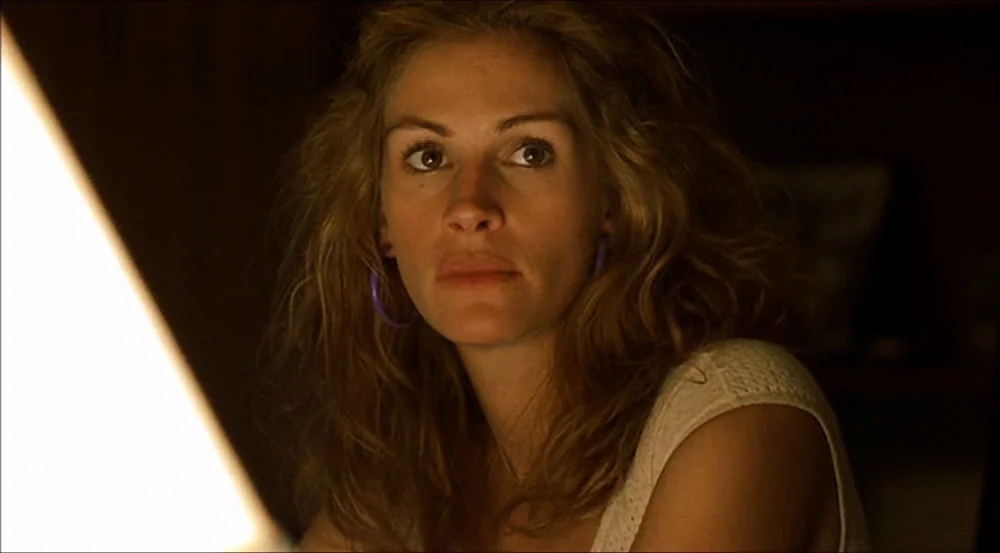Erin Brockovich (2000) movie still: closeup — A dark indoor space is dimly lit by a single off-screen practical light. A young woman with wavy hair…