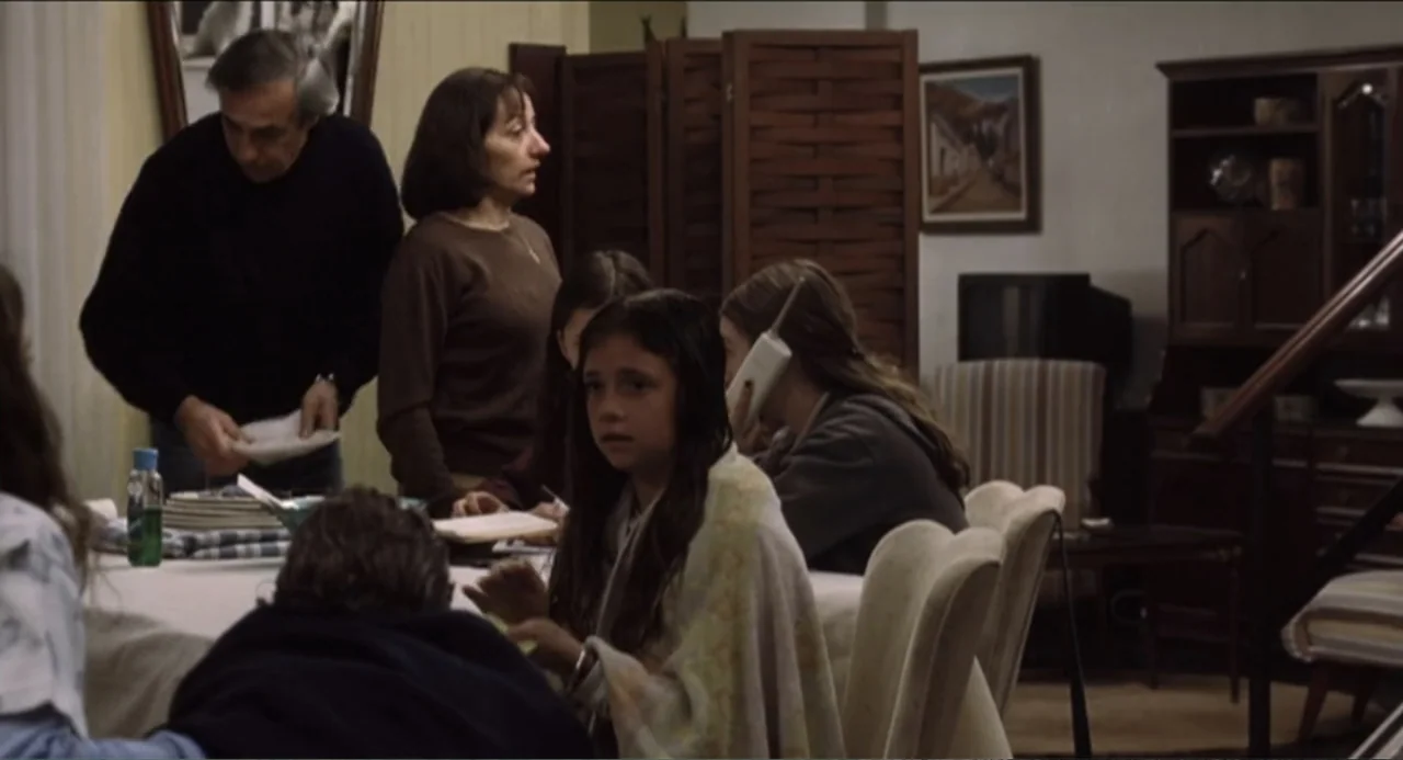 The Holy Girl (2004) movie still: medium — A residential dining room contains a wooden table, chairs, a hutch, and a room divider. Multiple family…