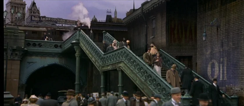 The House of Mirth (2000) movie still: wide — An early 20th century outdoor train station features an elaborate iron staircase and brick masonry.…