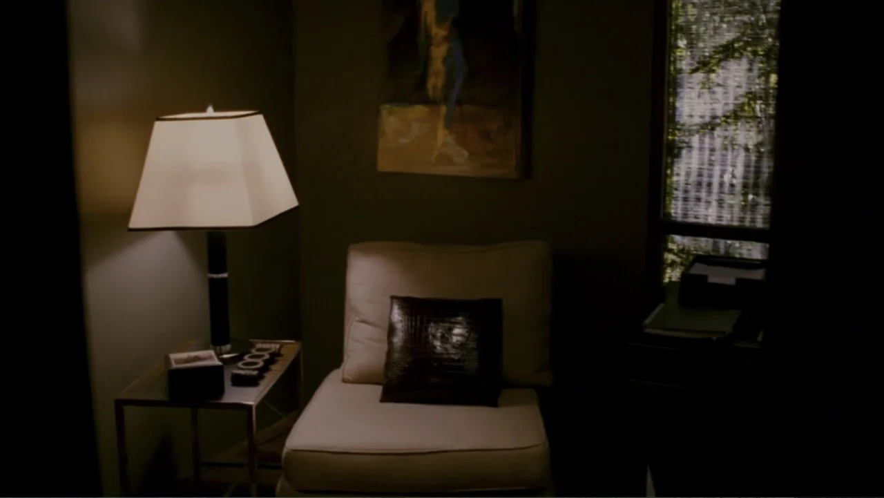 When a Stranger Calls (2006) movie still: medium — A corner of a room contains an armchair with a dark cushion beneath artwork. A lit lamp sits on a…