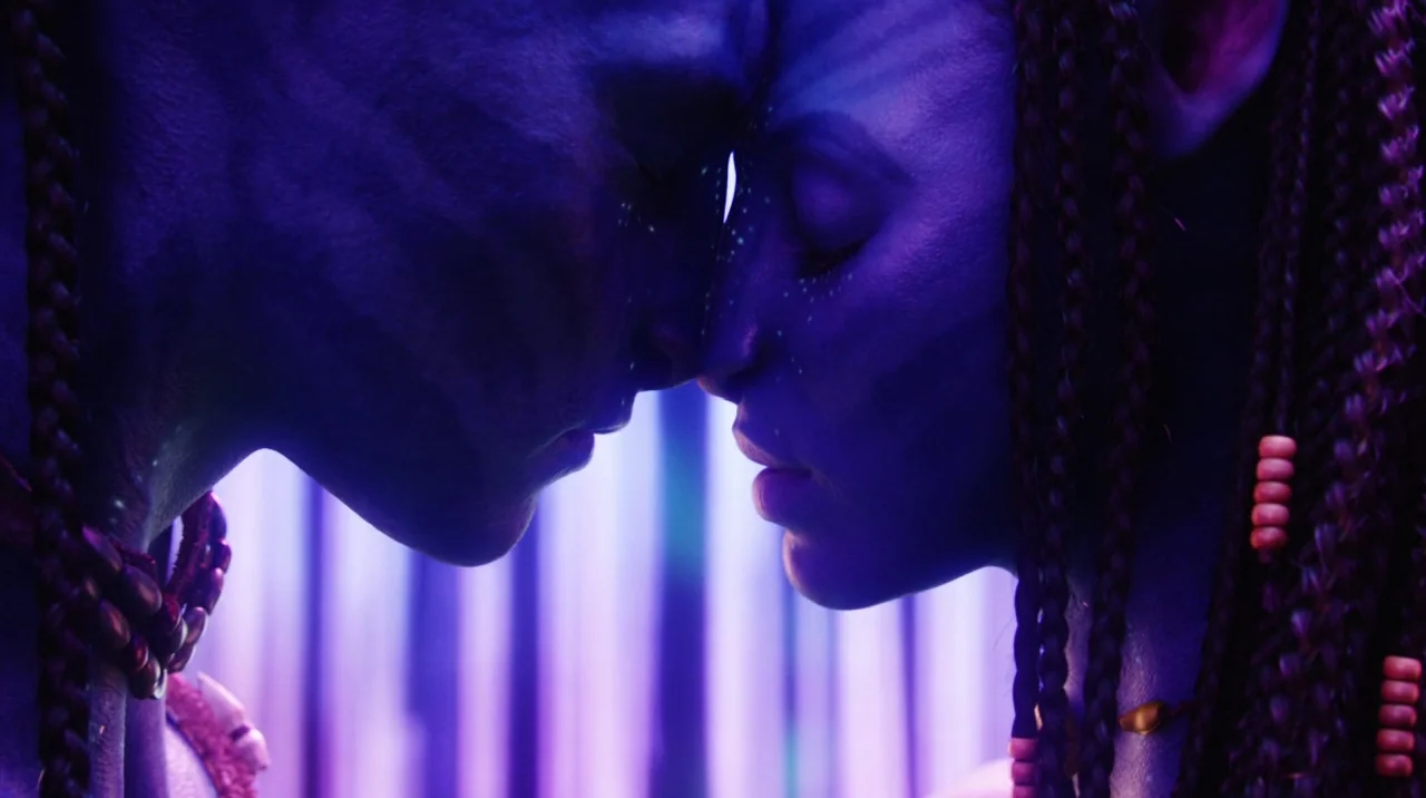 Avatar (2009) movie still: closeup — Two blue-skinned humanoid beings lean their foreheads against each other in low violet light. The pair stands…