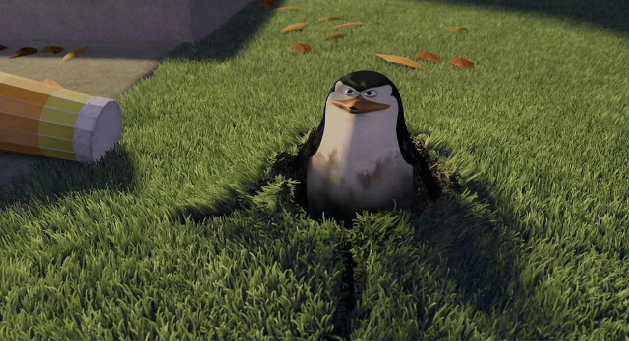 Madagascar (2005) movie still: medium — A green grass lawn contains a small hole with loose dirt edges. A penguin sits partially emerged from the…