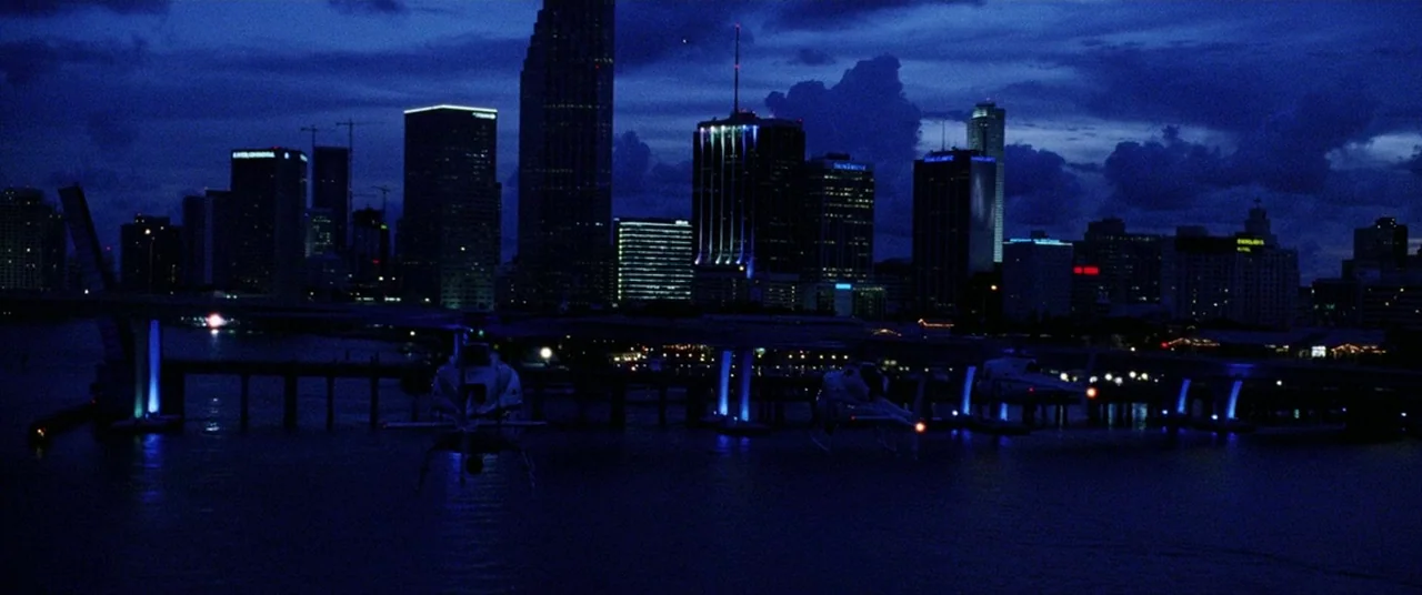 Bad Boys II (2003) movie still: establishing — A night view of the Miami skyline stretches across the horizon behind a bridge. Two helicopters hover…