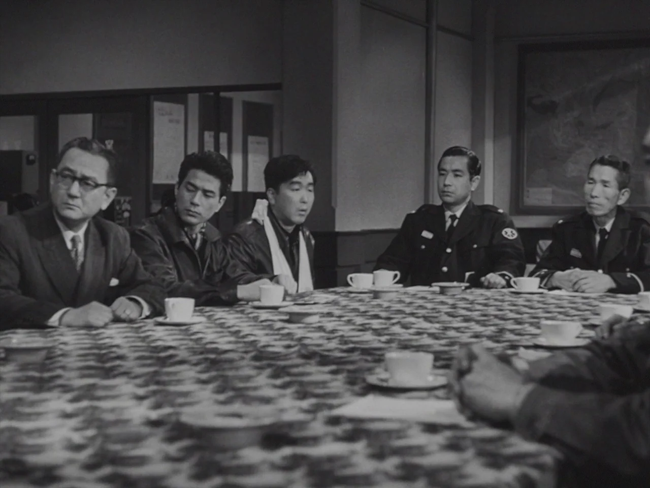Godzilla Raids Again (1955) movie still: medium — An interior conference room features five men seated around a large patterned tablecloth. They are…