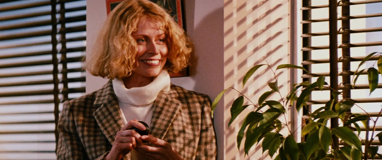 Razorback (1984) movie still: medium — An interior space with light passing through slatted blinds onto a white wall. A blonde woman in a blazer…