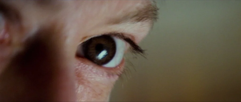 We Need To Talk About Kevin (2011) movie still: closeup — An extreme close-up view focuses on a human eye in a neutral setting. The eye looks…