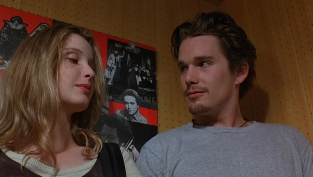 Before Sunrise (1995) movie still: medium — A wall covered in red paper posters with black and white imagery serves as background. A young man and…