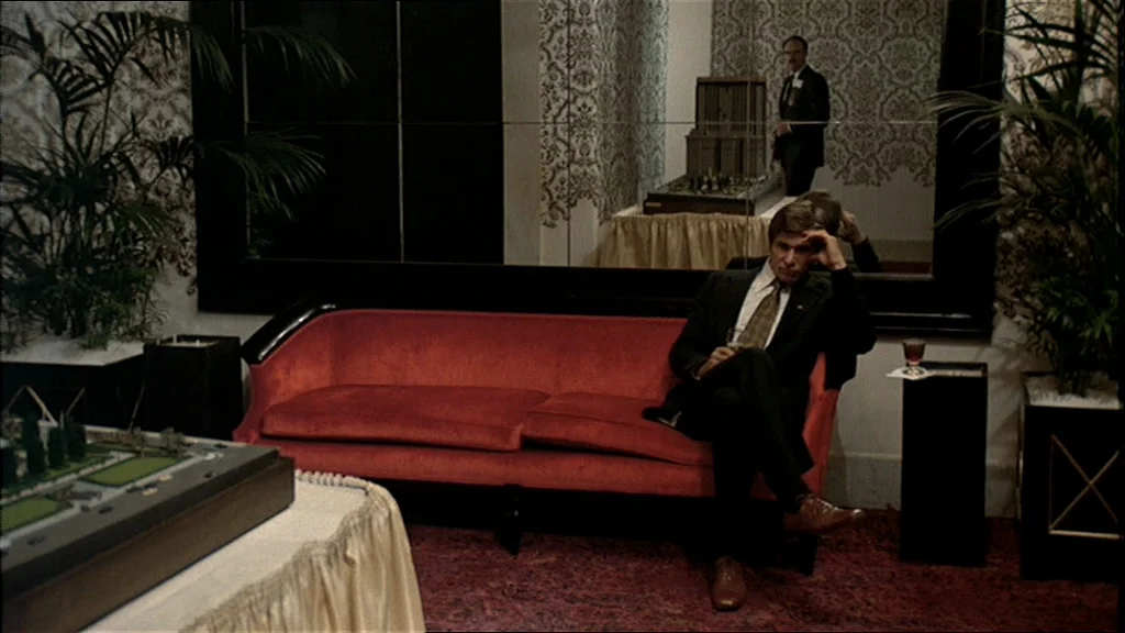 The Conversation (1974) movie still: medium — A sophisticated lobby features a red velvet sofa, ornate wallpaper, and large wall mirrors. A man in a…