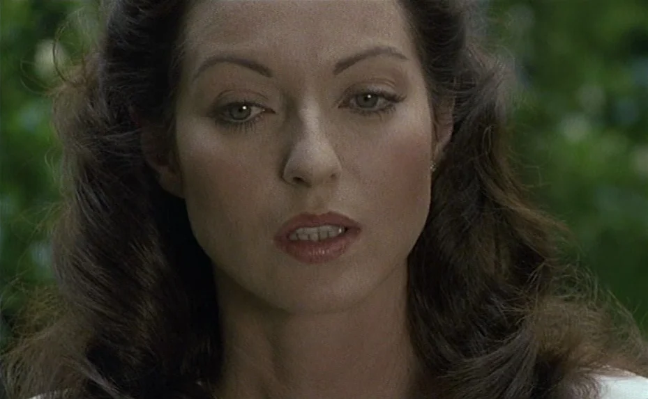 Love on the Run (1979) movie still: closeup — A woman stands in a lush green outdoor setting with bokeh foliage behind her. She maintains a frontal…