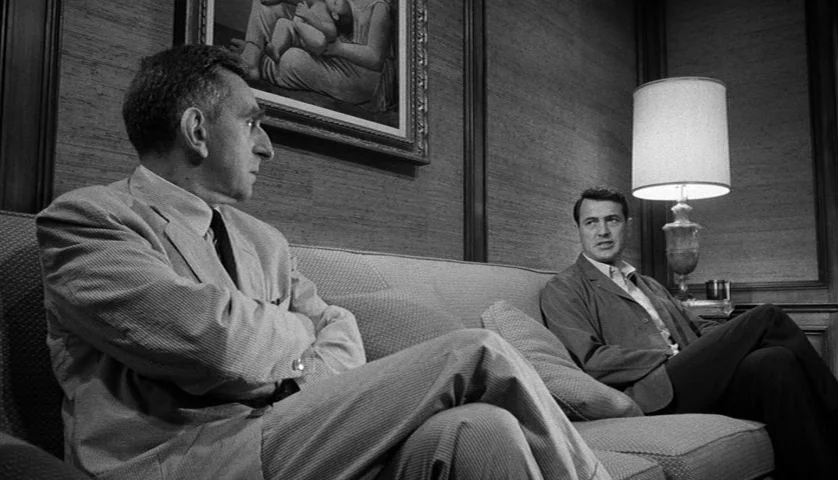 Seconds (1966) movie still: medium — A wood-paneled room contains a sofa and a wall-mounted framed painting of a woman. Two men sit together on the…