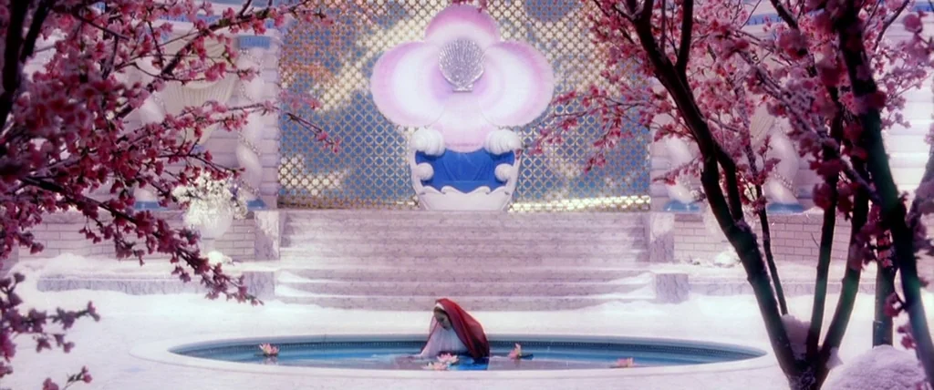 The Cell (2000) movie still: wide — A large outdoor courtyard features marble stairs leading to a stylized shell-shaped throne. A woman sits in a…
