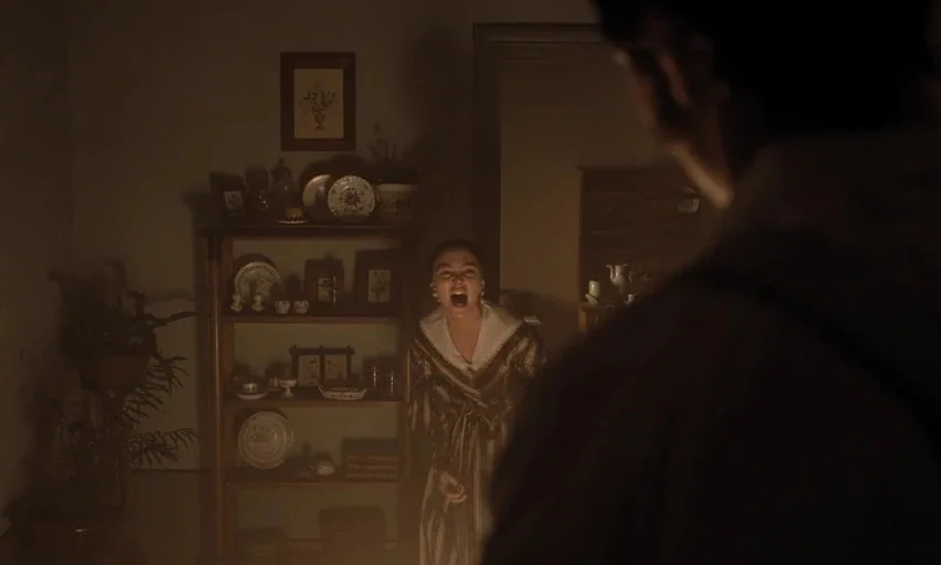 Nosferatu (2024) movie still: medium — A dimly lit room contains a wooden hutch filled with ceramic plates and decorative items. A woman in a period…