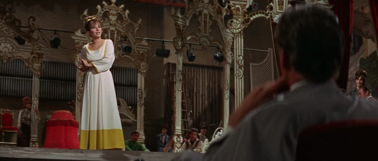 Funny Girl (1968) movie still: medium — A theatrical rehearsal space features ornate white scaffolding and a low wooden platform. A woman stands on…