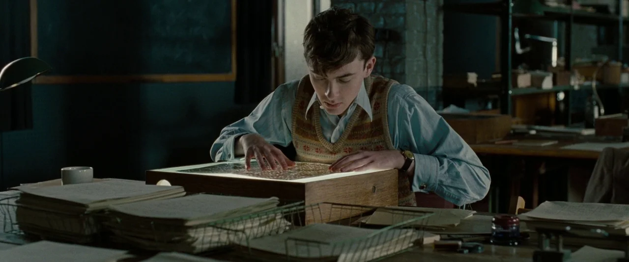 The Imitation Game (2014) movie still: medium — An office filled with stacks of papers and professional equipment at night. A young man examines…