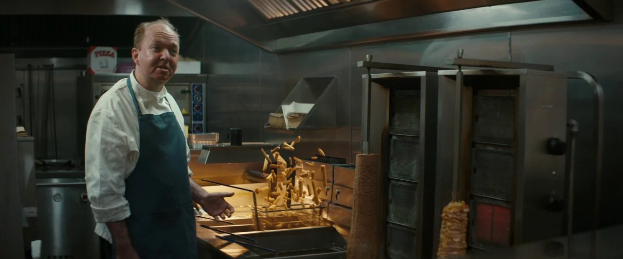 Extra Ordinary (2019) movie still: medium — A commercial fast-food kitchen features stainless steel fryers and a vertical rotisserie spit. A man in…