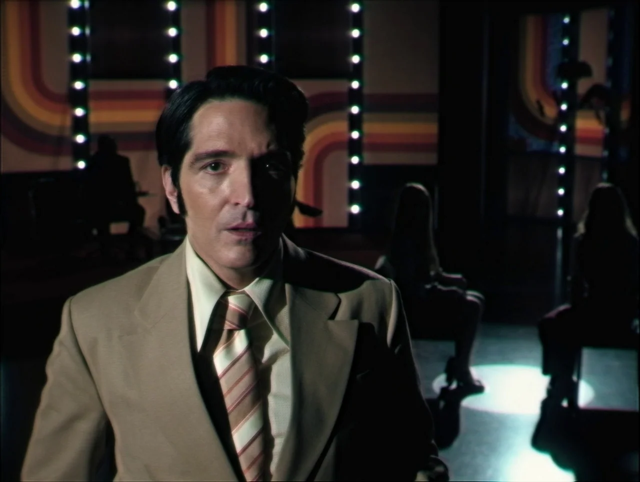 Late Night With The Devil (2023) movie still: medium — A television studio background features vertical arrays of lights and vibrant 1970s…