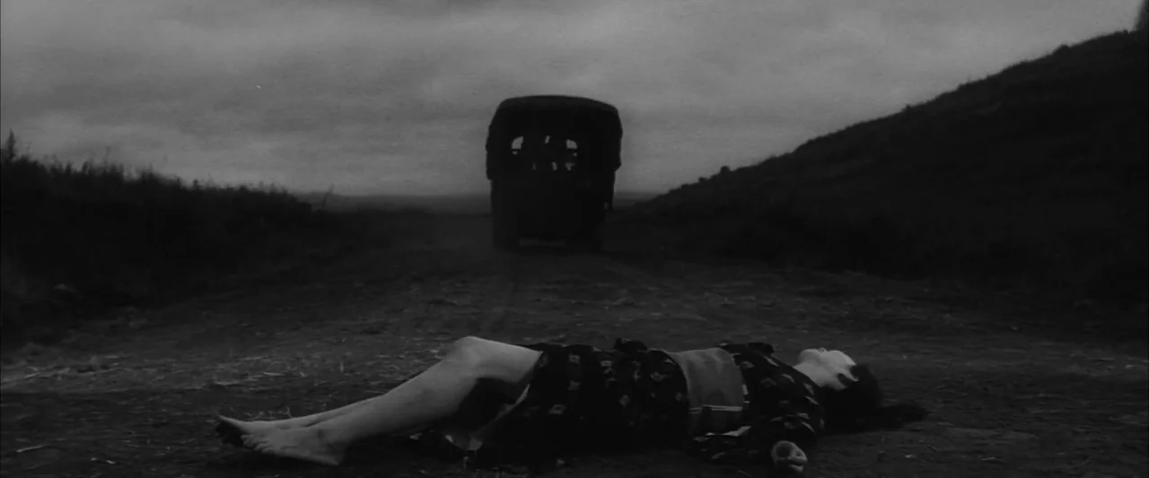 The Human Condition III: A Soldier’s Prayer (1961) movie still: wide — A dark, unpaved rural road stretches toward a distant vehicle under a cloudy…