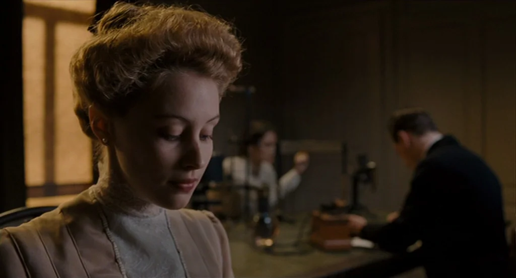 A Dangerous Method movie still: closeup — A dimly lit room with laboratory equipment including glassware on a wooden table. A young woman in a…