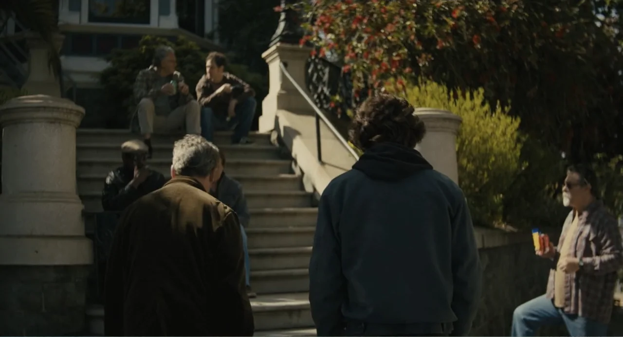 Beautiful Boy (2011) movie still: medium — A group of men congregates on the concrete stairs leading up to an old building. A man in a blue hoodie…