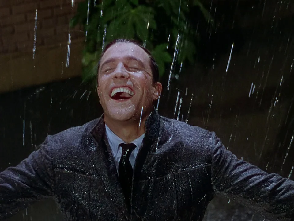 Singin’ in the Rain (1952) movie still: medium — A wet urban exterior at night with heavy rainfall falling against dark pavement. A man in a suit…