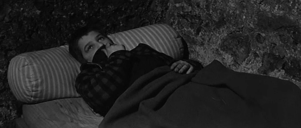 The 400 Blows (1959) movie still: medium — A dark stone room with a small, narrow bed placed against a rugged wall. A young boy lies under a blanket…