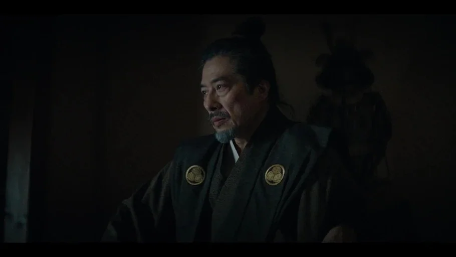 Shogun (2024) movie still: medium — A dimly lit room in a traditional Japanese structure features shadows and subtle textures. A middle-aged man in…