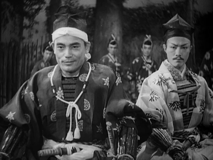 The Men Who Tread on the Tigers Tail (1945) movie still: medium — Two men in traditional samurai attire sit side-by-side in an outdoor wooded area.…
